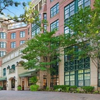 A multi-story urban building with a brick facade and large windows, surrounded by trees.