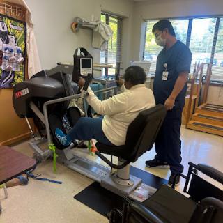 A patient engaging in physical therapy with the assistance of a therapist, using specialized exercise equipment.