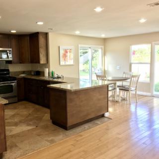 A modern kitchen with wood flooring, featuring a spacious kitchen island and dining area bathed in natural light.