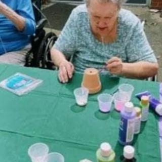 An elderly person painting a small pot at an outdoor crafting event.