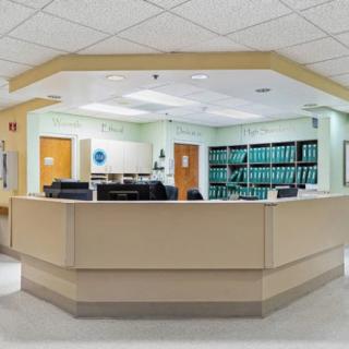 A hospital reception area with a central desk and shelves in the background.