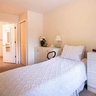 A minimalist bedroom featuring a single bed with white linens, a dresser, and neutral decor.