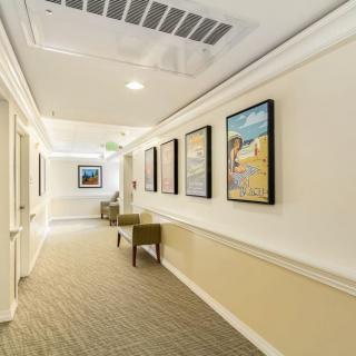 A well-lit hallway featuring framed artwork and chairs along a carpeted floor.