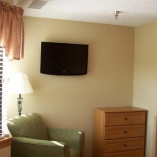 A simple room interior with a mounted television, chair, dresser, and lamp.