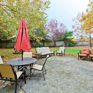 A cozy backyard patio with outdoor furniture and an umbrella, surrounded by autumn foliage.