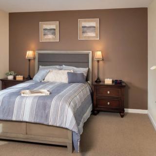 A cozy bedroom with a neatly made bed, nightstands, and lamps on either side, complemented by framed art on the wall.