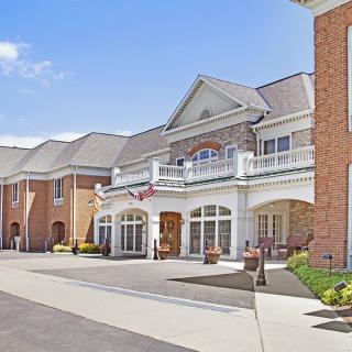 A large brick residential building with a grand entrance and landscaped surroundings under a clear blue sky.