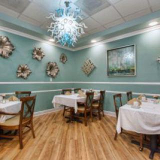 A cozy restaurant interior with elegantly set tables, decorative wall art, and a modern chandelier.