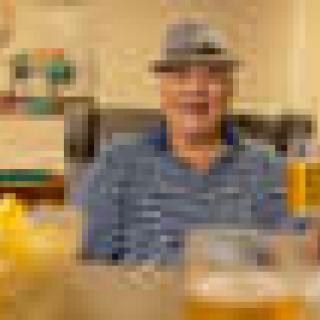 A man wearing a hat sits at a table with drinks in a restaurant.