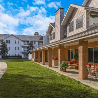 Exterior view of a residential building with a patio and green lawn under a blue sky.