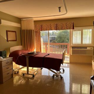 A hospital room with a bed by the window illuminated by sunlight.