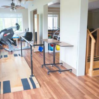A home workout area with a treadmill and adjustable desks on a hardwood floor.