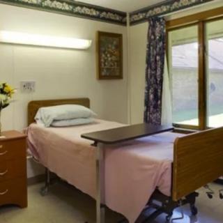 A hospital room with a neatly made patient bed and a small bedside table under a window.