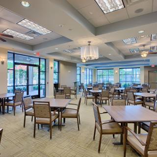 An empty dining area with tables and chairs, illuminated by natural light and ceiling fixtures.
