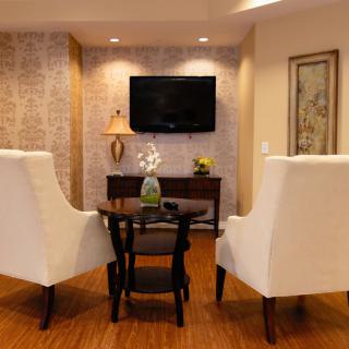 A cozy living room setup featuring two elegant chairs and a small wooden table, with a wall-mounted television and artistic decor.