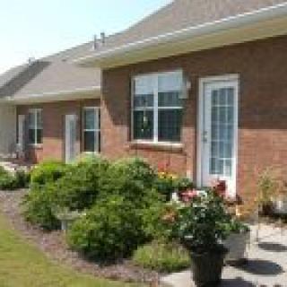 A well-maintained garden in front of a brick house with large windows and French doors.