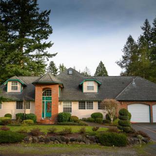 A suburban house with a brick exterior, surrounded by landscaped greenery and trees.