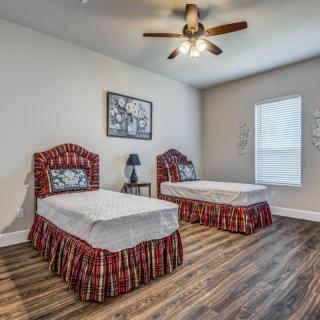 A neatly arranged bedroom with two twin beds, a wooden floor, and a ceiling fan.