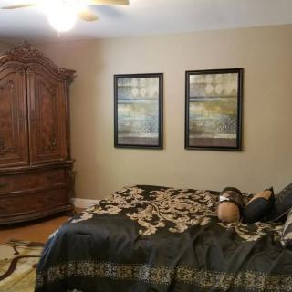 A cozy bedroom with an ornate wooden armoire, a bed covered with a patterned comforter, and two framed artworks on the wall.