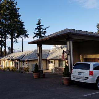 A view of a motel with an adjacent parking lot and surrounded by tall trees.