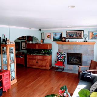 A cozy living room with a fireplace, hardwood floors, and various artworks on the walls.