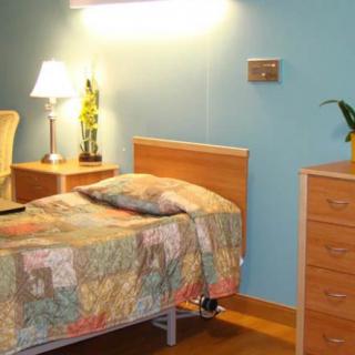 A cozy bedroom with a wooden bed and dresser, illuminated by a bedside lamp.