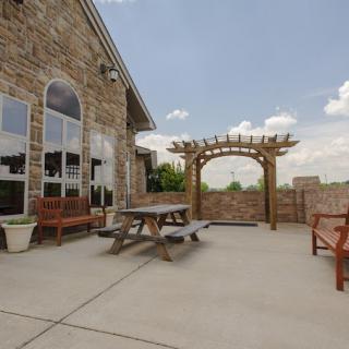 A stone patio with a picnic table and benches, featuring a pergola under a cloudy sky.