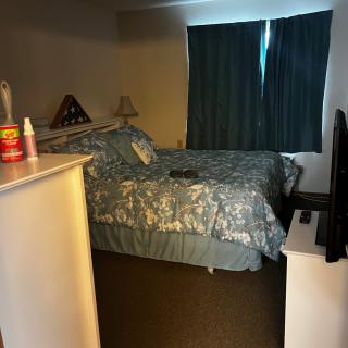 A cozy bedroom with a patterned bedspread, closed curtains, and a television on a stand.