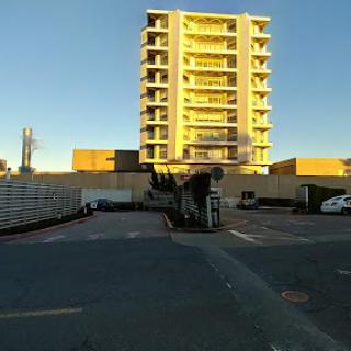A modern apartment building bathed in sunlight, with a parking area in the foreground.