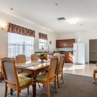 A cozy dining area connected to a small kitchen, featuring a wooden table and chairs with ample natural light.