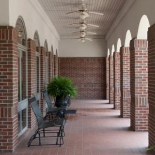 A brick corridor with arches and ceiling fans, featuring outdoor furniture and potted plants.