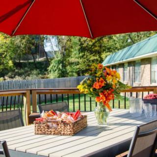 A sunny backyard patio with a table set with flowers and a basket under a red umbrella.