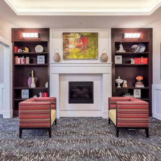 A modern living room with a central fireplace, surrounded by built-in shelves and colorful chairs.