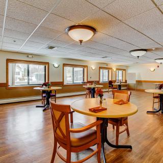 A spacious dining area with wooden tables and chairs, featuring large windows and ceiling lights.