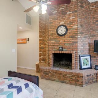 A cozy interior space featuring a brick fireplace, wall-mounted clock, and ceiling fan with a nearby bed.