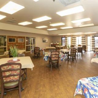 A well-lit dining area with multiple tables and chairs, featuring large windows and wooden flooring.