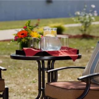 A cozy outdoor seating area with a small table, two chairs, and a pitcher of water on the table, surrounded by a peaceful garden setting.