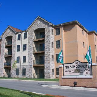 A modern apartment building with a welcoming entrance sign and neatly landscaped surroundings.