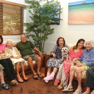 A group of seniors sitting on a couch together in a living room, enjoying each other's company with a small dog.