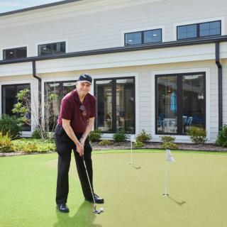 A person playing golf on a putting green in front of a house.