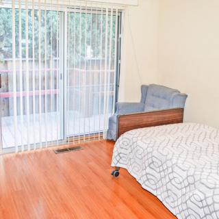 A bright bedroom with a single bed, wooden flooring, and a sliding glass door leading outside.