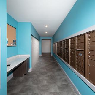 A modern mailroom with blue walls and multiple mailboxes along the hallway.