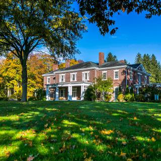 A brick mansion surrounded by autumn foliage on a bright, sunny day.
