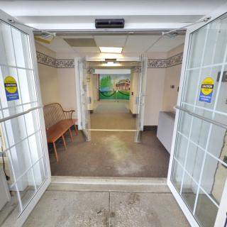 Entrance to a building with an open door leading to a corridor and waiting area.