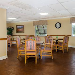 A well-lit dining area with wooden tables and chairs, decorated with artwork and a wall clock.