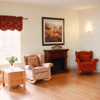 Cozy living room with armchairs and a fireplace, adorned by a painting and natural light streaming through the window.