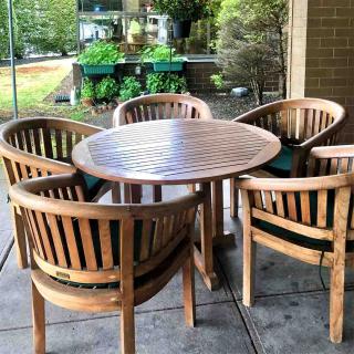 A set of wooden patio furniture with a round table and five chairs.