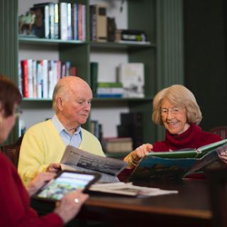 A group of elderly individuals enjoying a moment together while reading and discussing books at a cozy indoor setting.