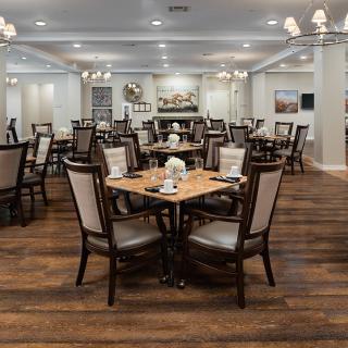 An elegant restaurant dining room with neatly arranged tables and chairs, wooden flooring, and chandeliers.