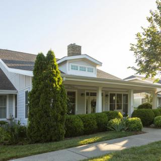 A charming residential house with a porch, surrounded by a well-maintained garden and trees.